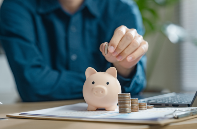 人が豚の貯金箱に硬貨を入れている。